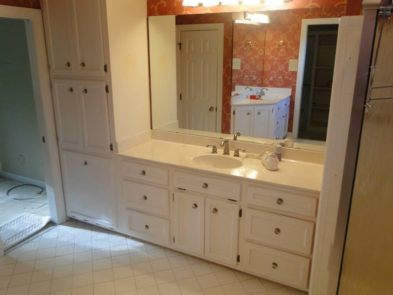 Dated bathroom vanity and mirror with patterned wallpaper before renovation