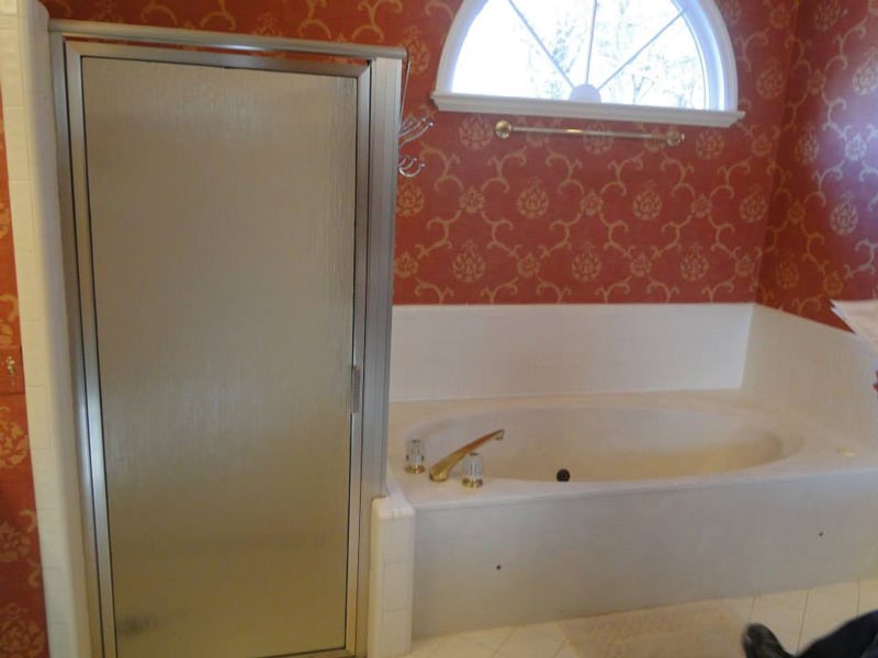 Dated bathroom with a red accent wall and builder tub before renovation