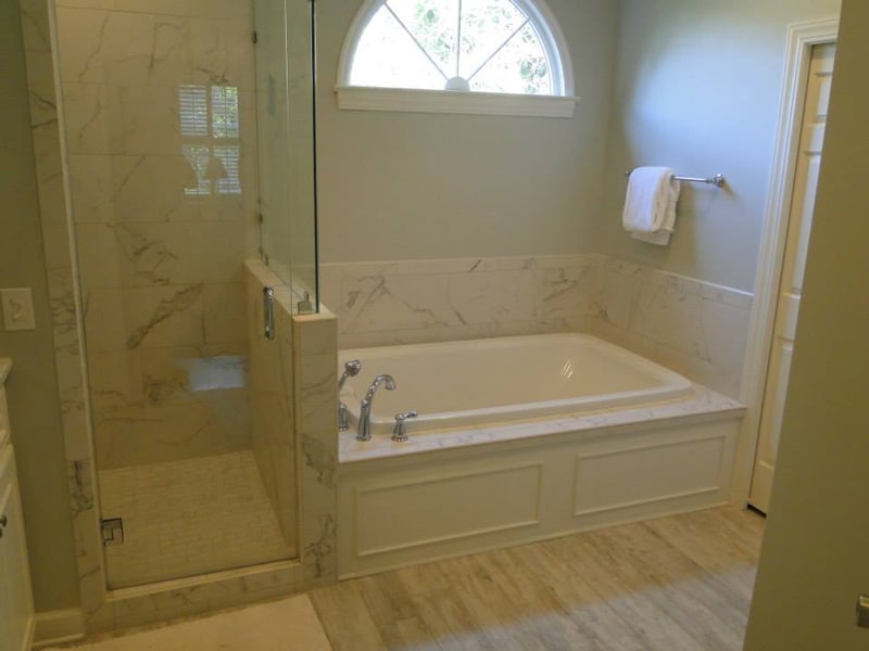 Renovated master bath with a tiled soaking tub beneath an arched window