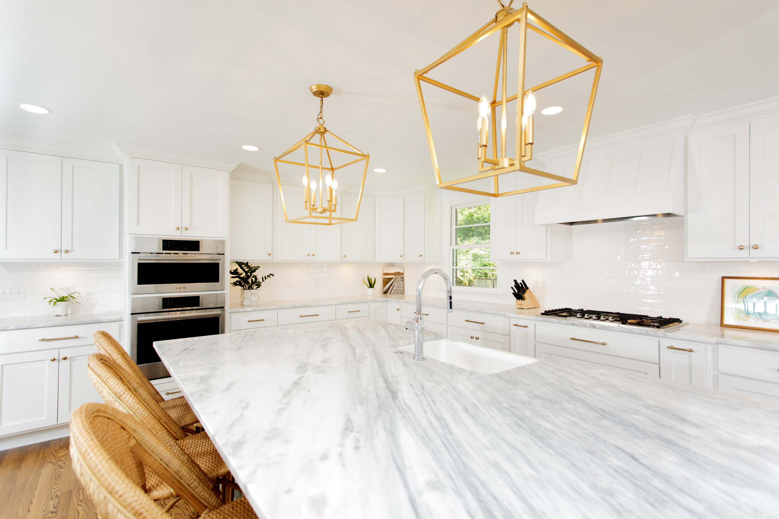 Remodeled white kitchen with a marble island and brass lantern pendants