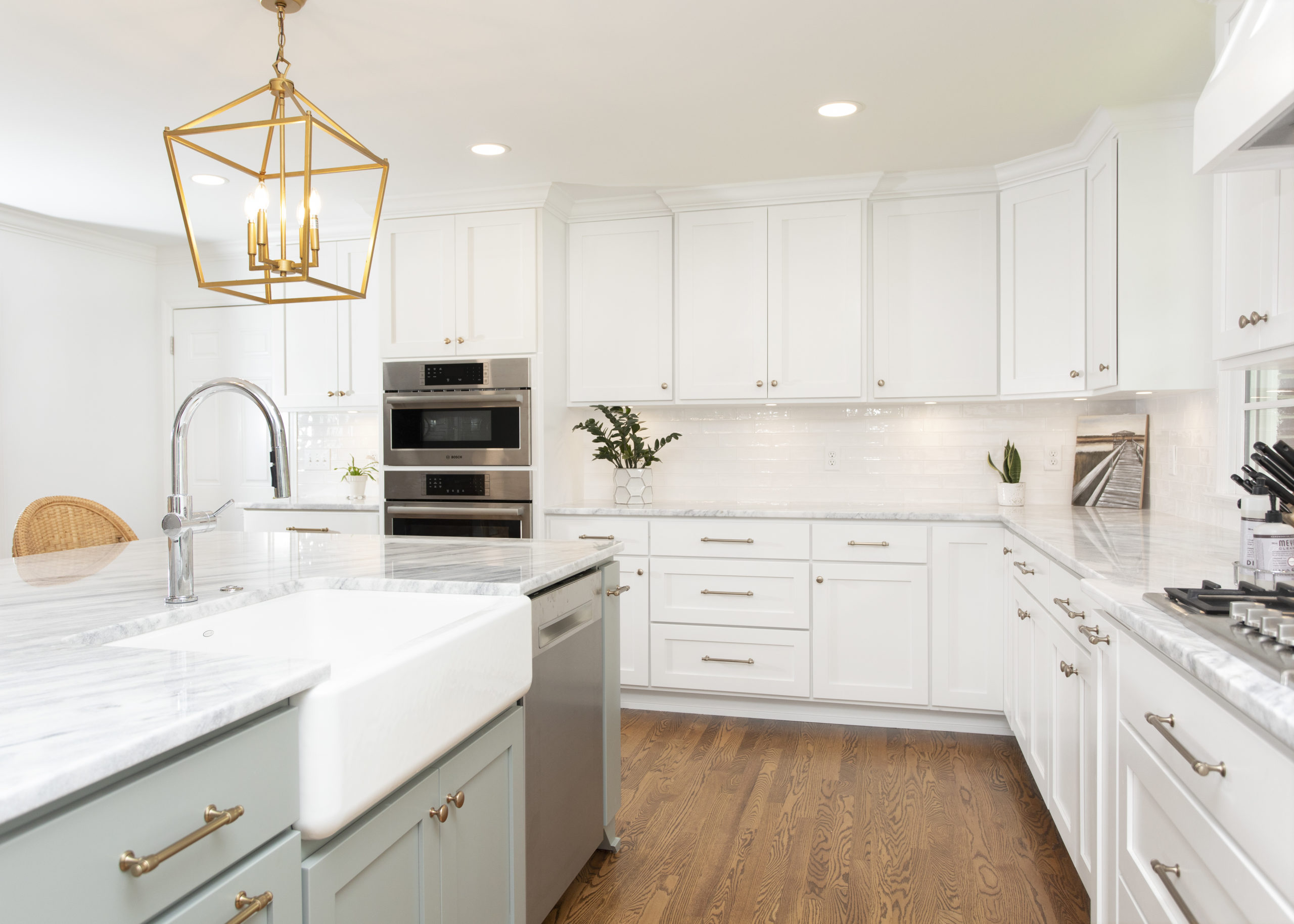A bright remodeled kitchen with a marble island, brass lantern pendants and stainless appliances by Palmetto Construction & Renovations