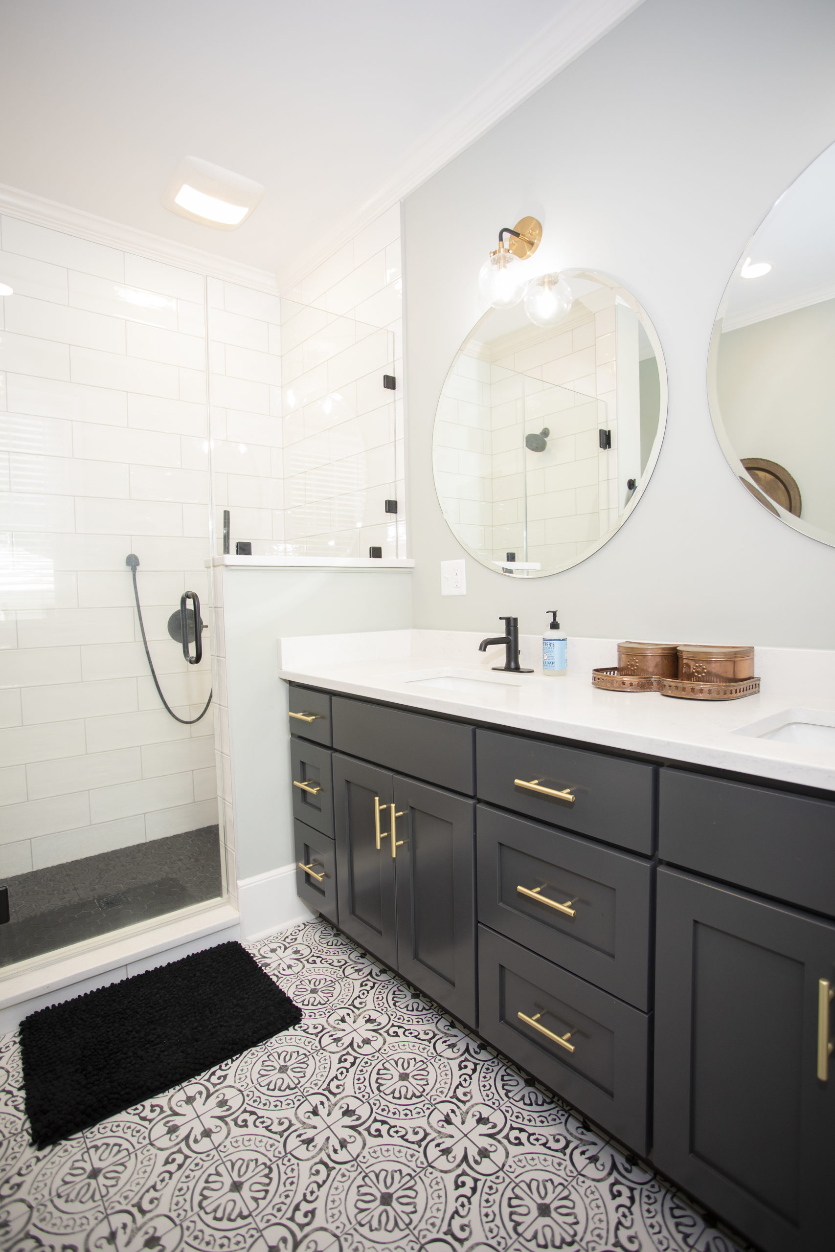 Bathroom with a dark vanity, round mirror and brass fixtures